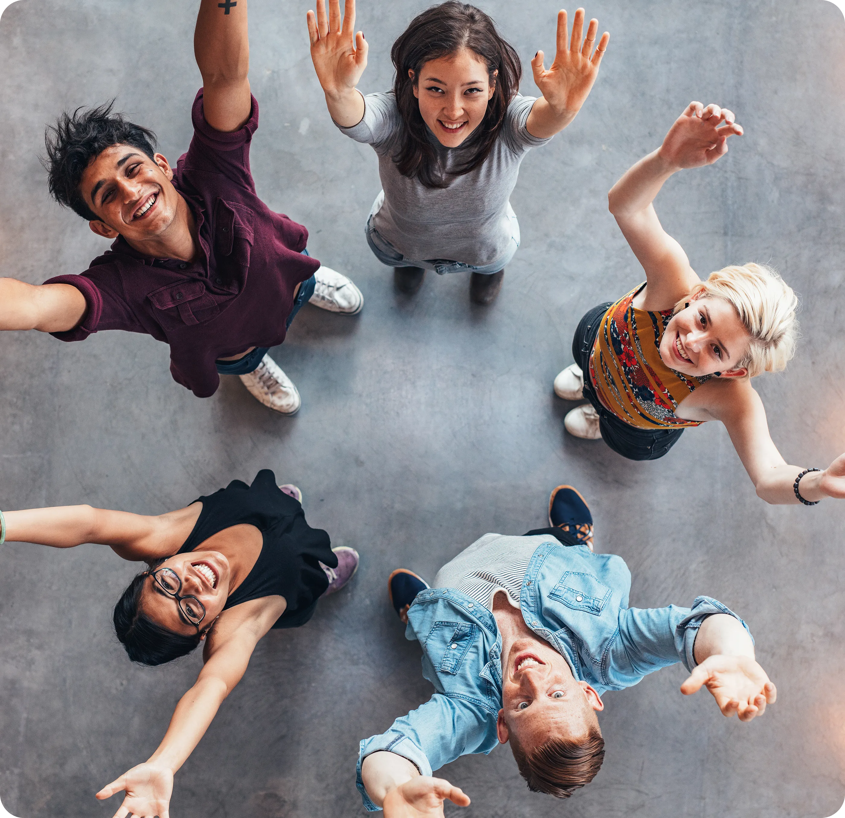 Five people standing in a circle look up with arms raised, smiling at the camera. They are on a grey background.